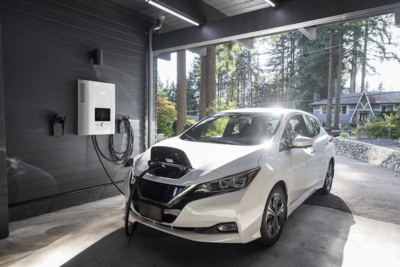 a white electric vehicle is charging from a wall charger in a garage with the garage door open